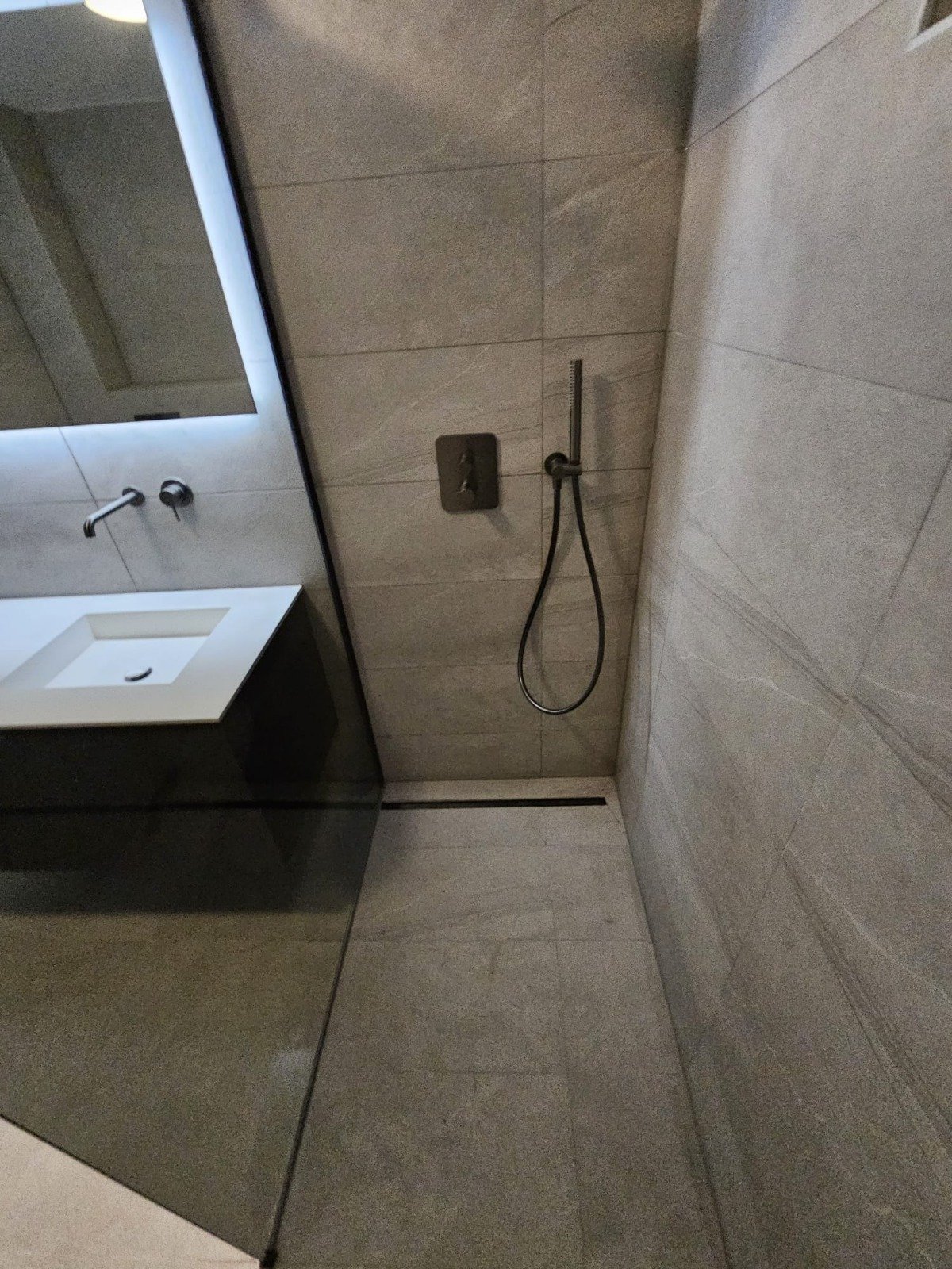 Moderne badkamer met inloopdouche, van vloer tot plafond betegeld met grijze tegels, wastafel met spiegel boven