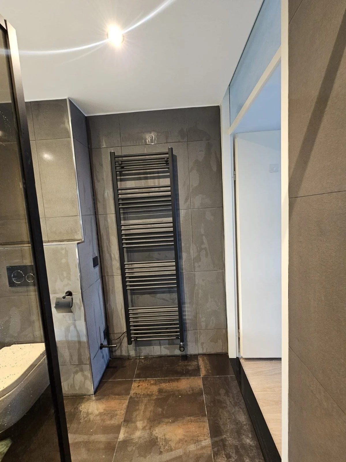 Een badkamer met grijze tegels, een zwart handdoekenrek en een witte deur.