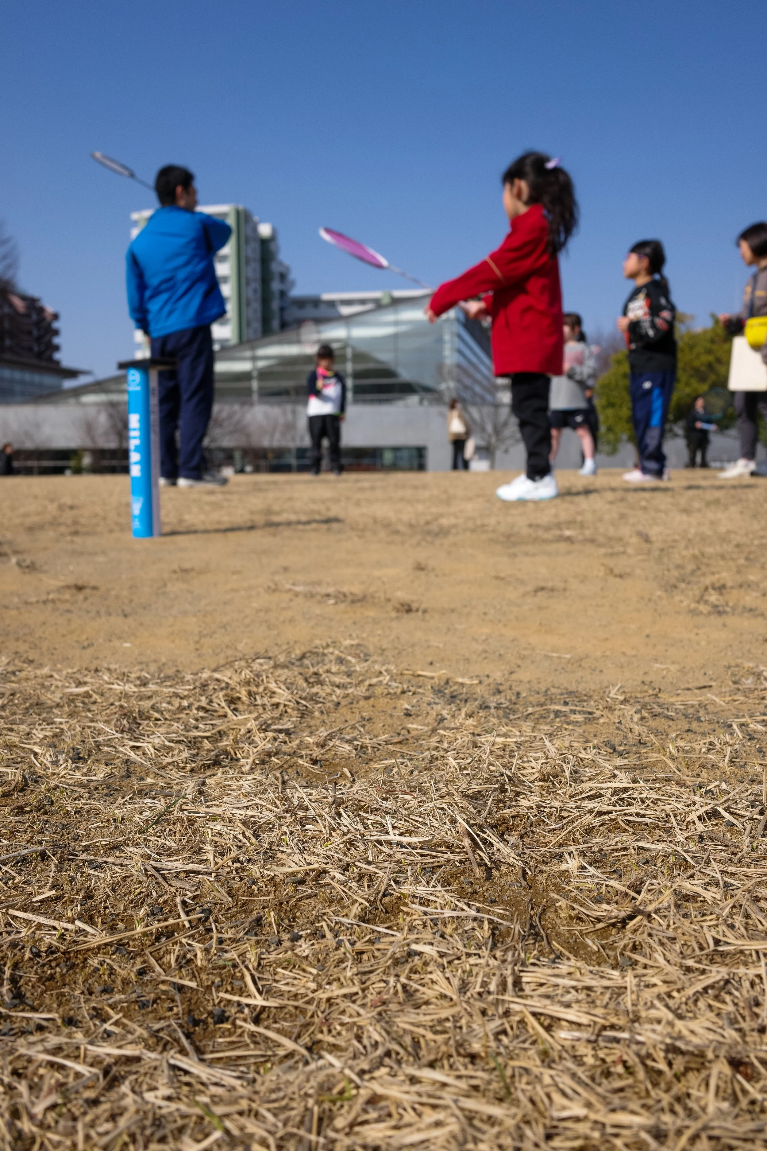 子供たちが外でシャトルコックを使ってバドミントンをしている様子。青空の下、複数の子供と大人が参加している。」}}#jetbrains_icon#important_notes: - 最も基本的な行動と場所を端的に説明してください。 - キャプション内に具体的な人物、場所、またはブランドは含めないでください。 - 3つの要素があれば十分です。 - できるだけ簡潔に。 - 利用できる情報だけを使用します。 - 画像の内容をしっかりと伝える必要がある。 - 必要なら、色や服装も加える。 - 日本語で明確に表現してください。 これらのルールに従ってください。 もし不明点があれば、「不明です」とだけ回答してください。 それ以外の場合は、上のフォーマットに従ってください。 例：{