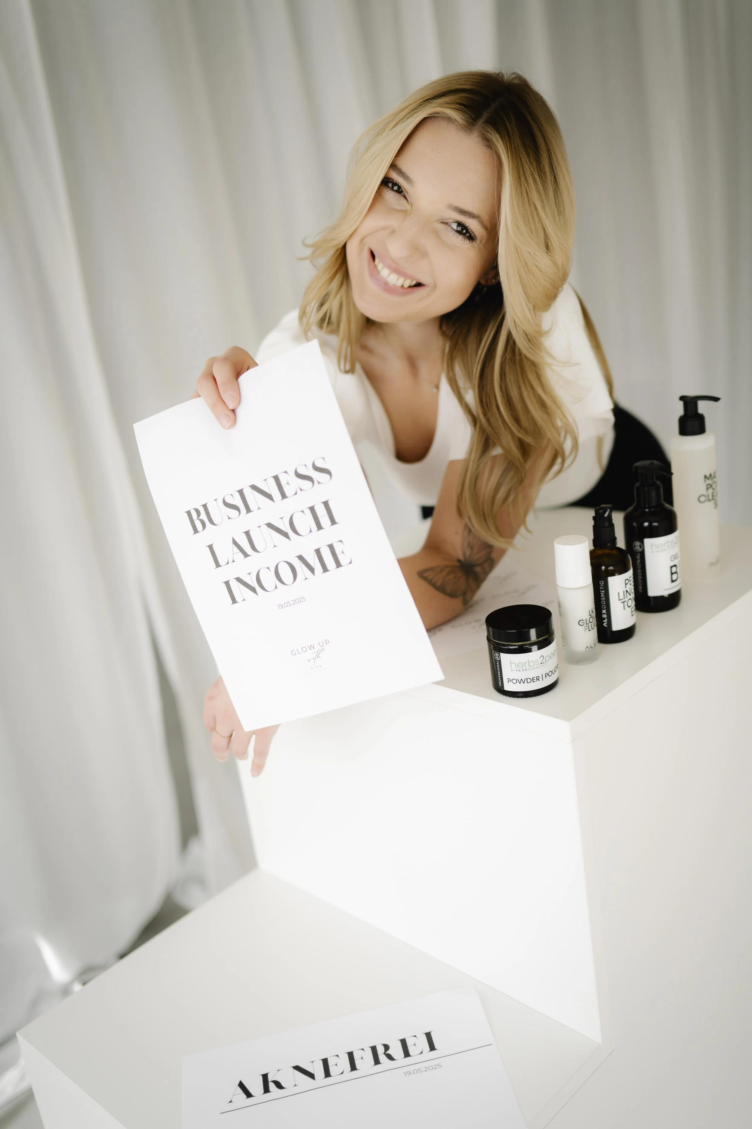 Eine lachende Frau mit langen blonden Haaren hält ein Papier mit der Aufschrift 'Business Launch Income'.