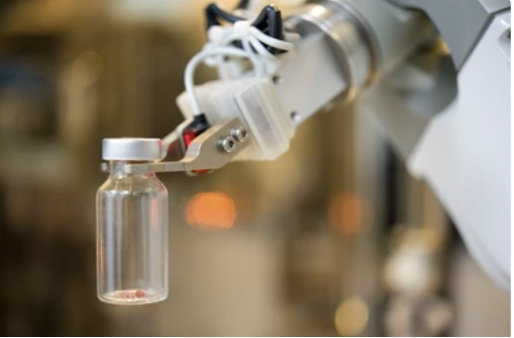 A robotic arm handling a small glass vial in a laboratory or manufacturing setting.
