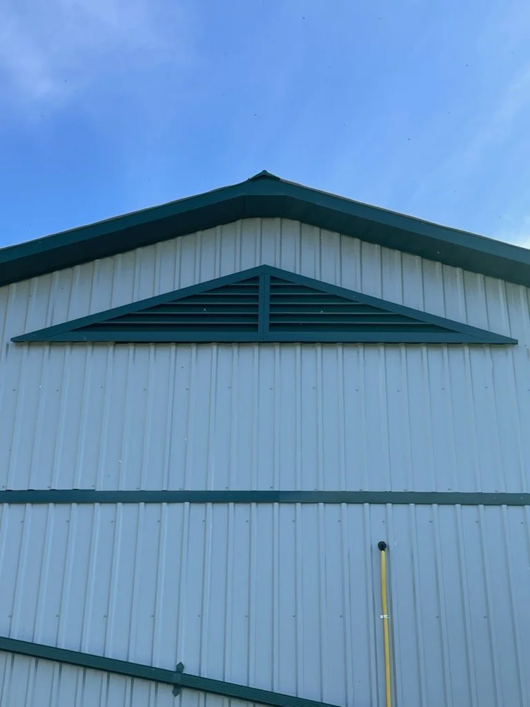 Front view of a white metal building with teal accents and a gable roof, set against a blue sky.