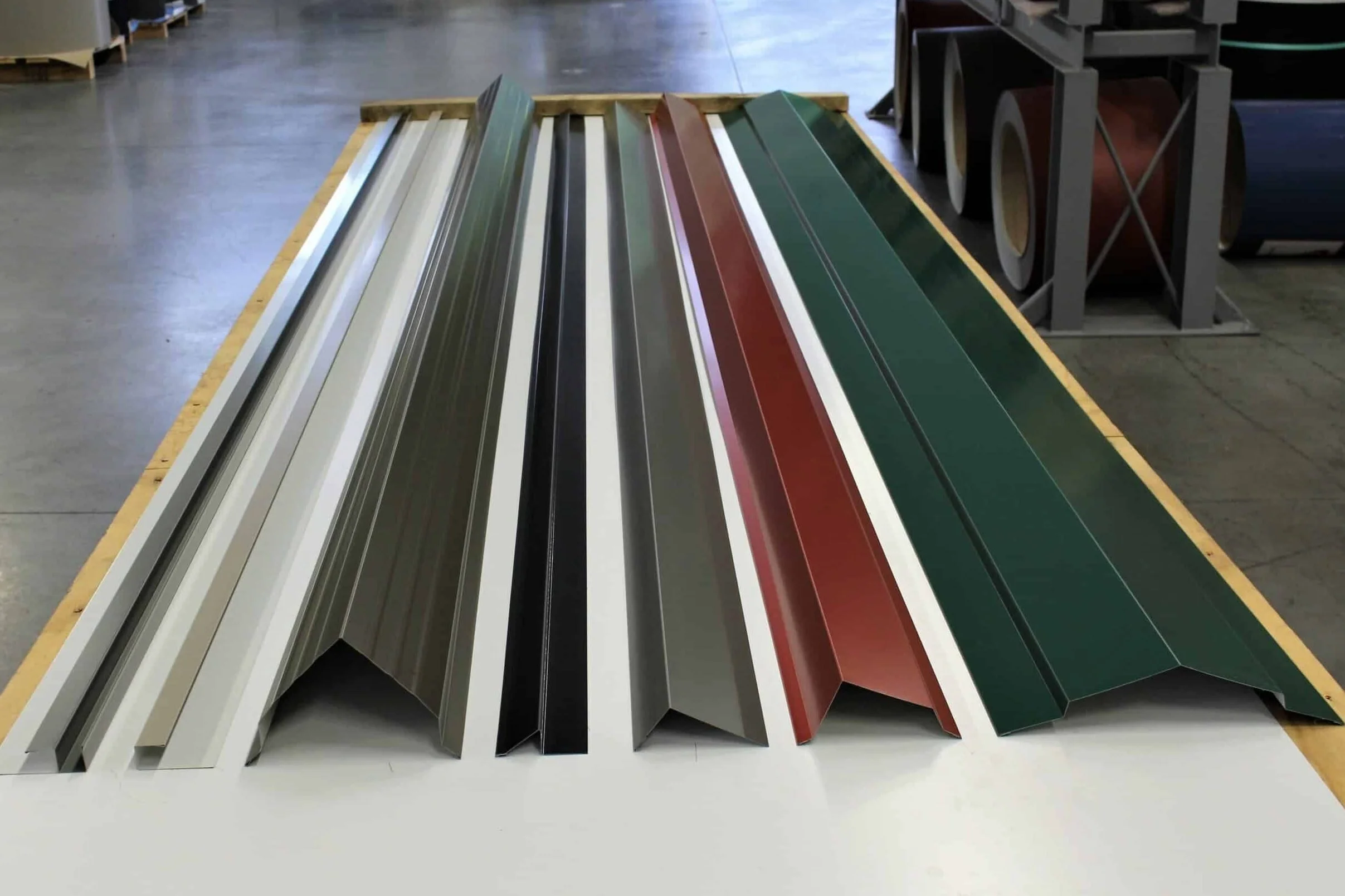 Various colored metal roofing panels arranged on a white table in a warehouse.