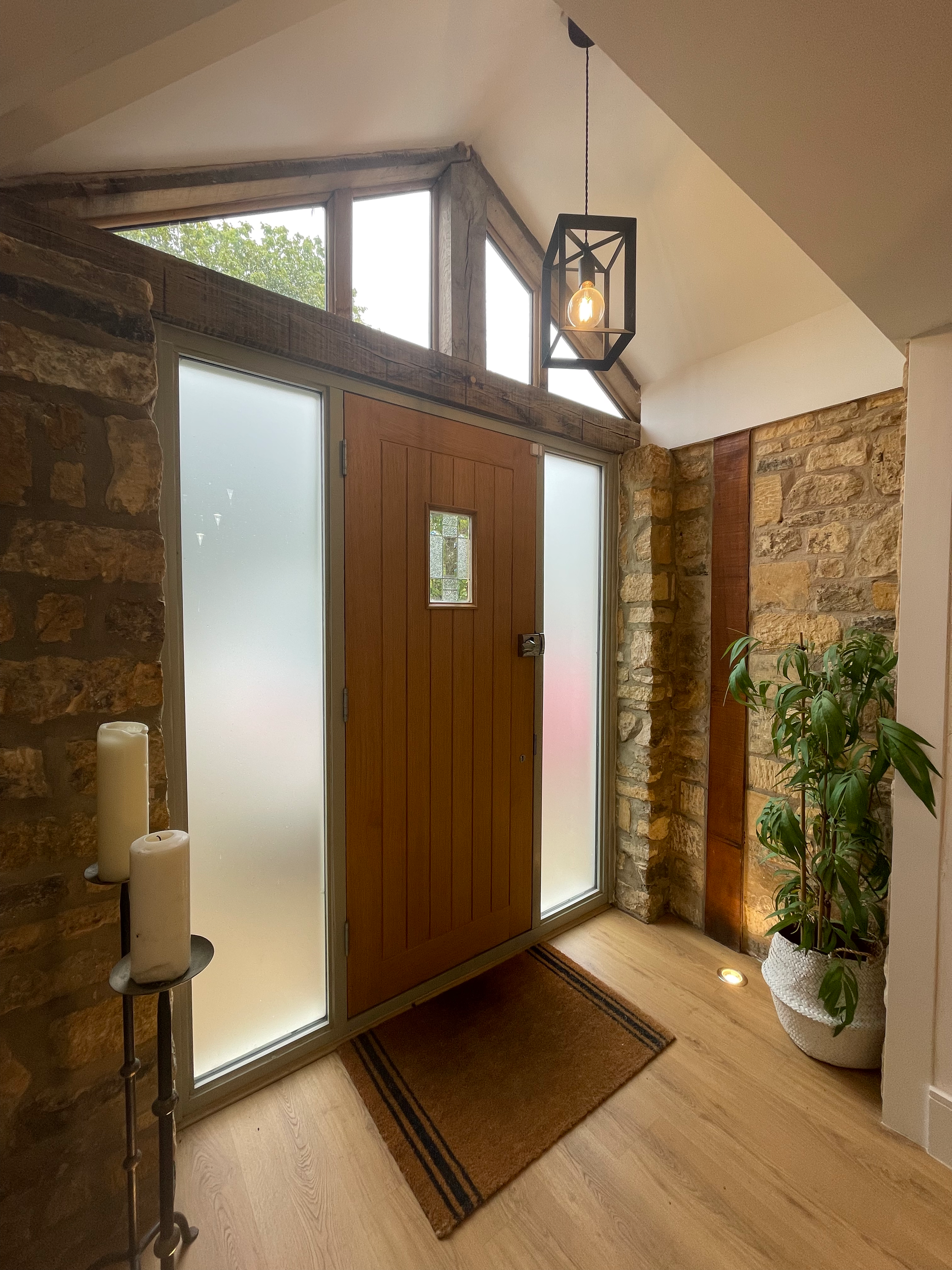 Entrance door with frosted glass panels, stone walls, potted plant, candles, and modern light fixture in a rustic-style interior.