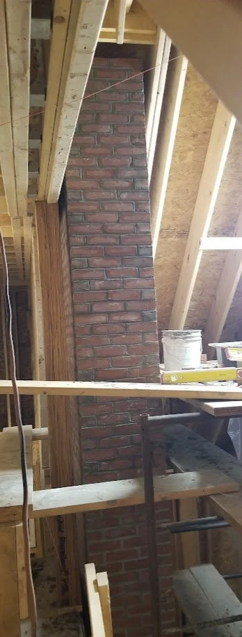 Construction site with a newly built brick chimney surrounded by unfinished wooden framing and construction tools.