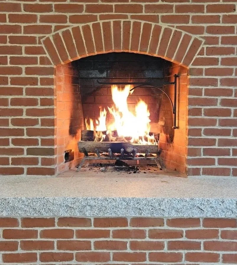 A fireplace with glowing flames burning wood logs inside a brick mantel.