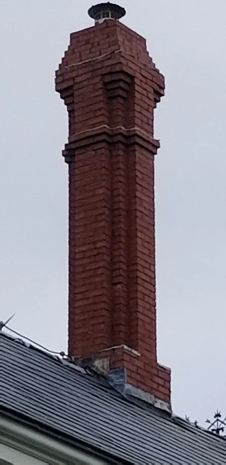 A tall, decorative red brick chimney on a rooftop against a gray sky.