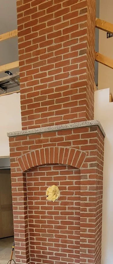 Brick fireplace with a chimney under construction, with yellow insulation foam inside the fireplace opening.