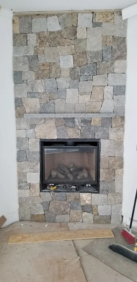 A fireplace with a stone facade under construction, with tools and construction materials nearby.