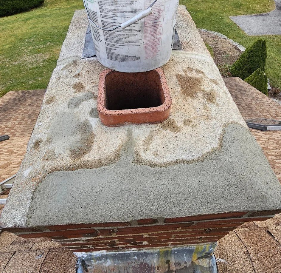 Close-up image of a chimney top with a new layer of cement being applied around the brick lining, with a container of mortar or cement placed on top.