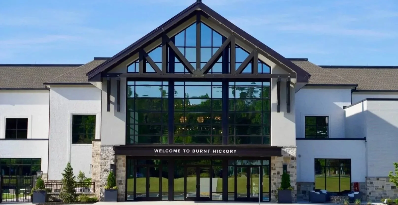 A modern building with a large glass entrance, stone accents, and a sign that says "Welcome to Burnt Hickory."
