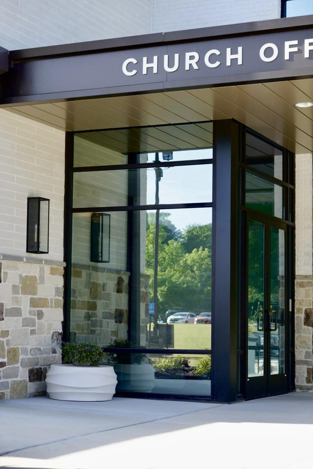 Entrance to a church office building with large glass windows and a black sign that reads 'CHURCH OFFICE'