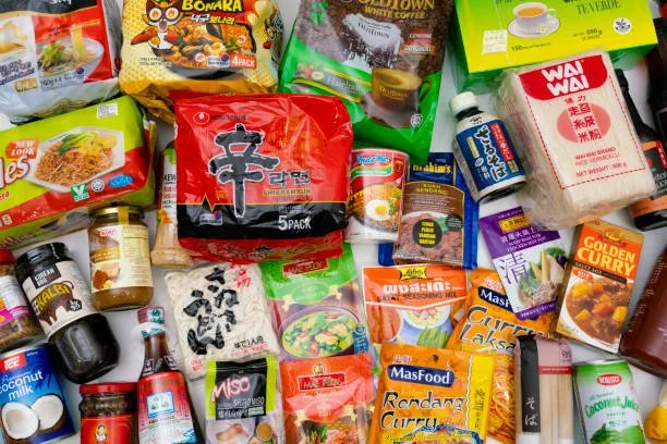 Verschiedene asiatische Lebensmittel und Gewürze, darunter Instant-Nudeln, Curry, Kokosnussmilch, Sojasauce, Tofu, Reis und andere Verpackungen.