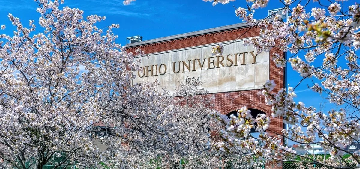 Ohio University campus scene with blooming cherry blossom trees and a brick building with the Ohio University sign.