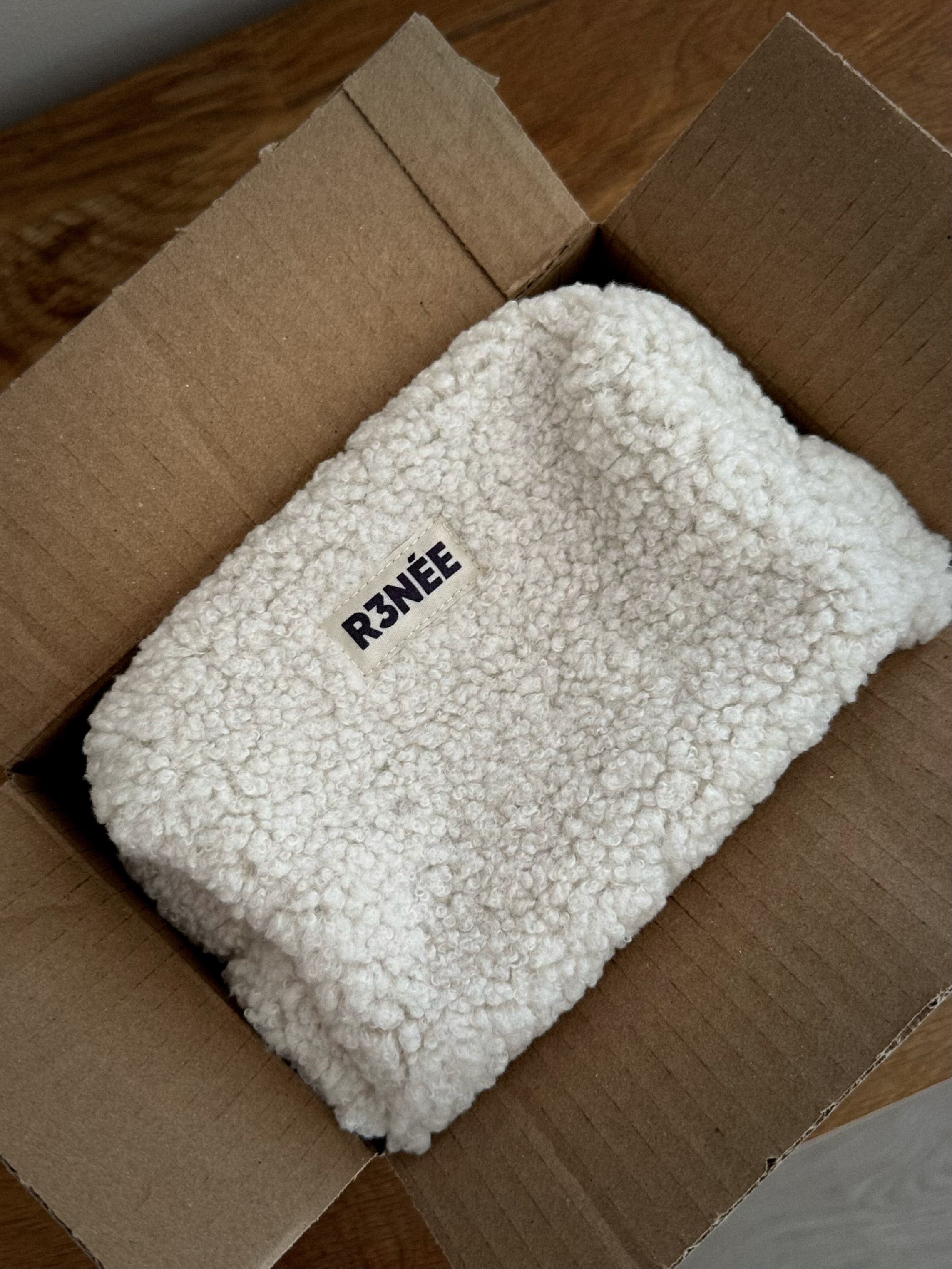 Une pièce en tissu blanc épais en forme de bourse dans une boite en carton.