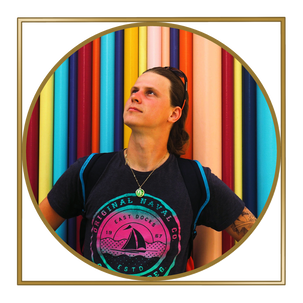Person with shoulder-length dark hair and tattoos, wearing a black T-shirt with a colorful graphic, standing in front of a vibrant background of vertical colored poles.