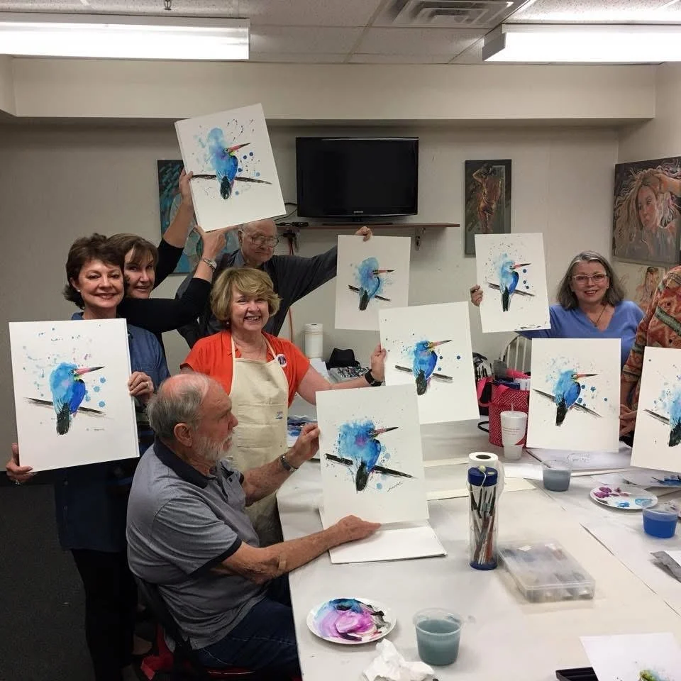 Group of people holding paintings of a blue bird with a colorful background in an art studio.