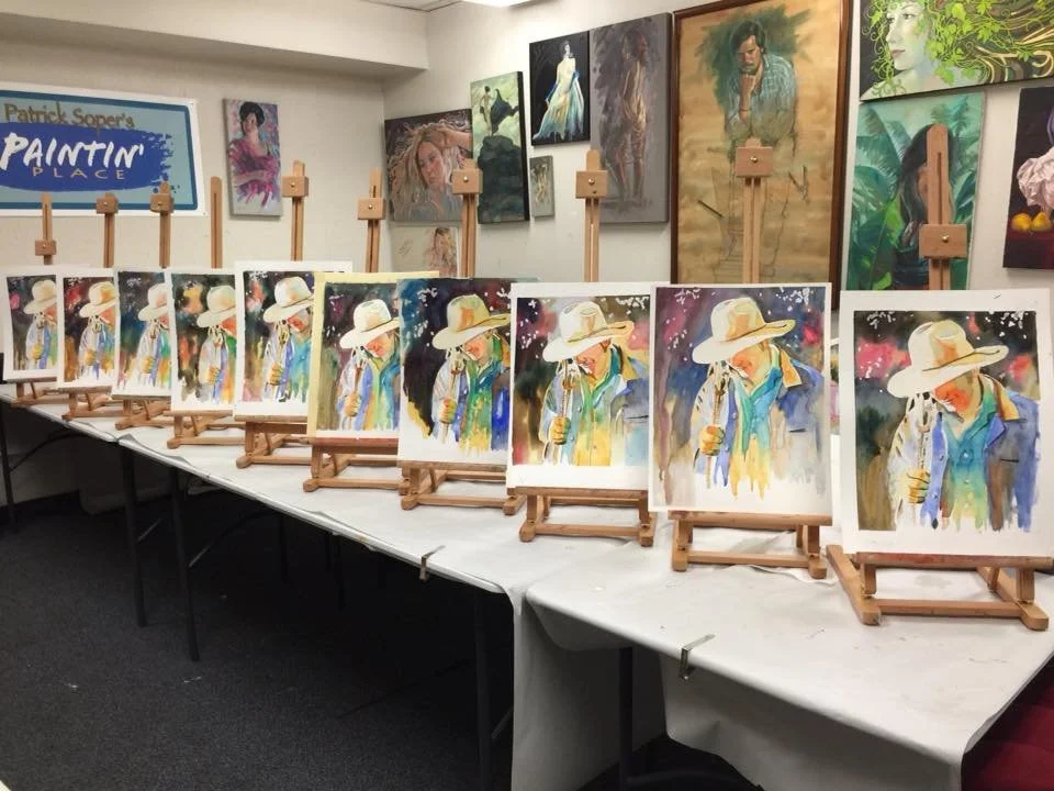 A series of watercolor paintings of a cowboy wearing a wide-brimmed hat and colorful clothing, displayed on small wooden easels on a table at an art studio.