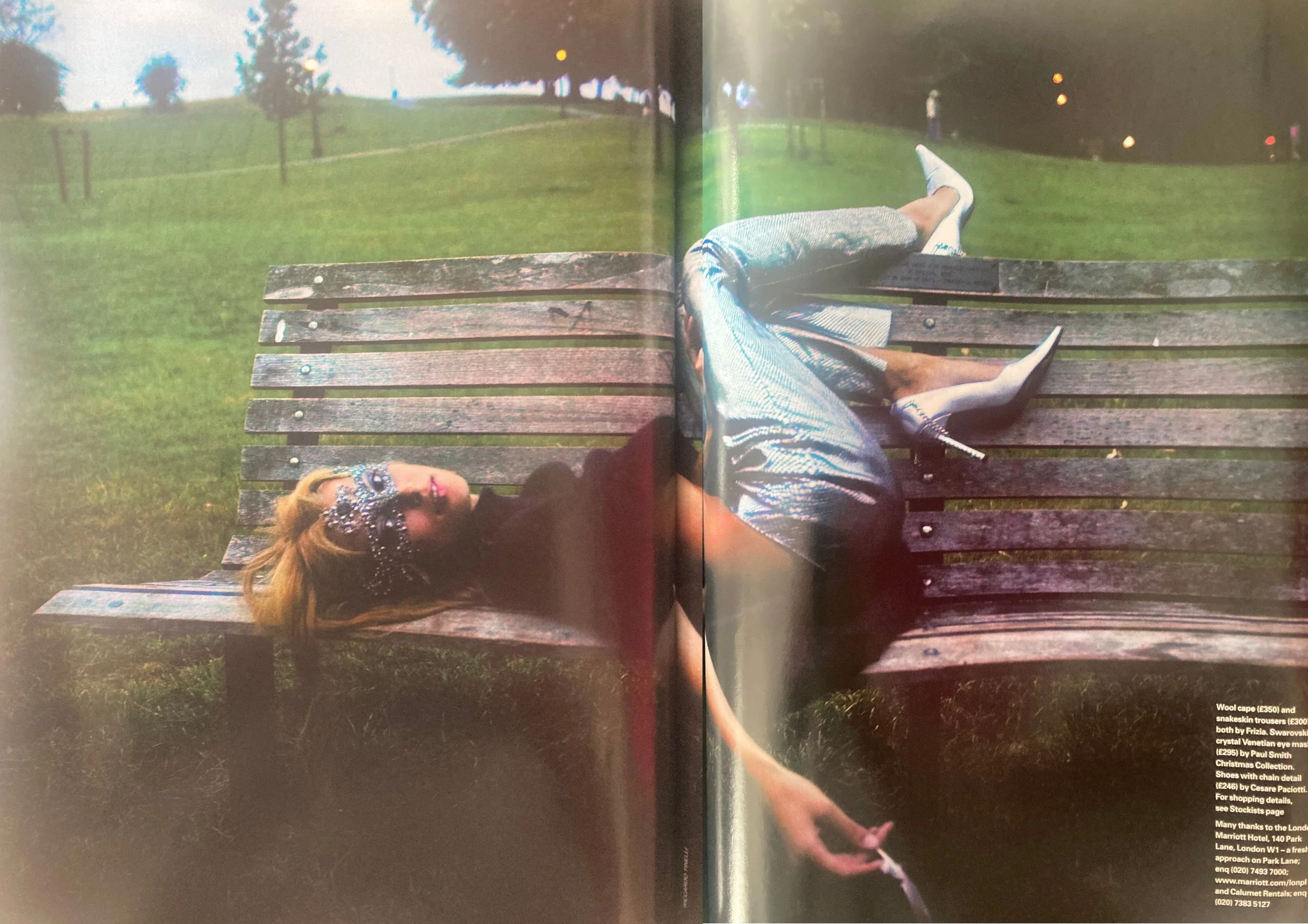 Double page fashion editorial from ELLE UK December 2003 showing a white woman with long blonde hair wearing blue metallic jeans and a black top with sequins on her face while laying on a park bench