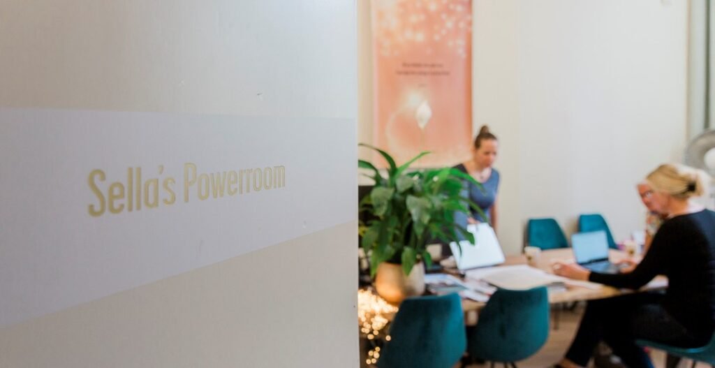 De foto toont een vergaderruimte met mensen die werken aan laptops, met een deurlabel dat zegt 'Sellál's Powerroom'.