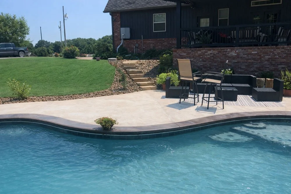 Backyard with a kidney-shaped swimming pool, patio furniture, and a raised deck with stairs leading to a grassy lawn and house.