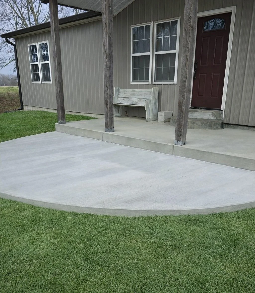 Front porch with concrete steps, a wooden bench, and a red front door on a house with gray siding. The porch is supported by wooden posts, and there's a neatly maintained lawn.