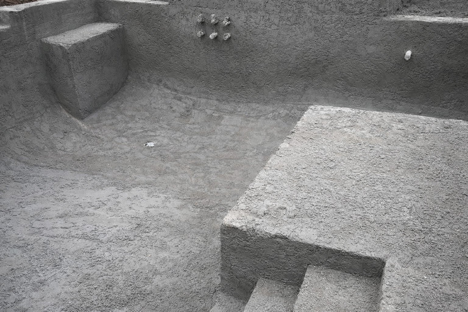 Close-up of a concrete hot tub with stepped seating area and textured surface in a backyard or patio setting.