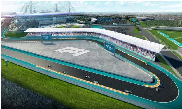 A futuristic race track with multiple cars, surrounded by green grass, and a large stadium in the background with a glass roof.