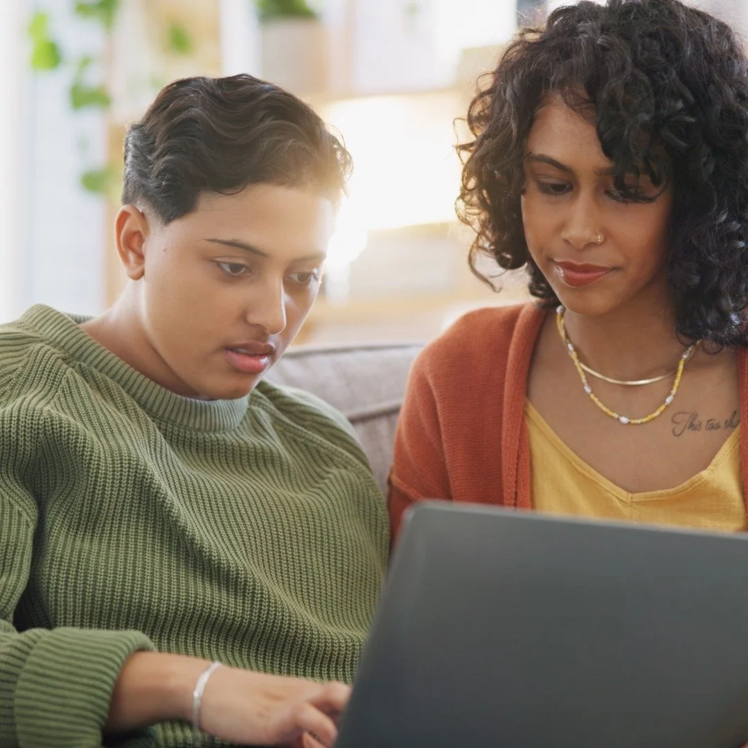 Two people sitting close together looking at a laptop screen at home while talking to their therapist.