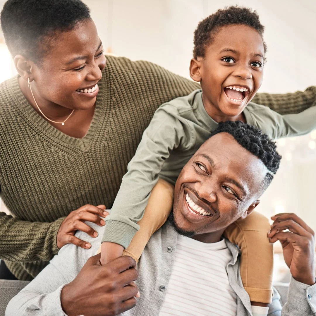 Family of three smiling and playing together indoors.