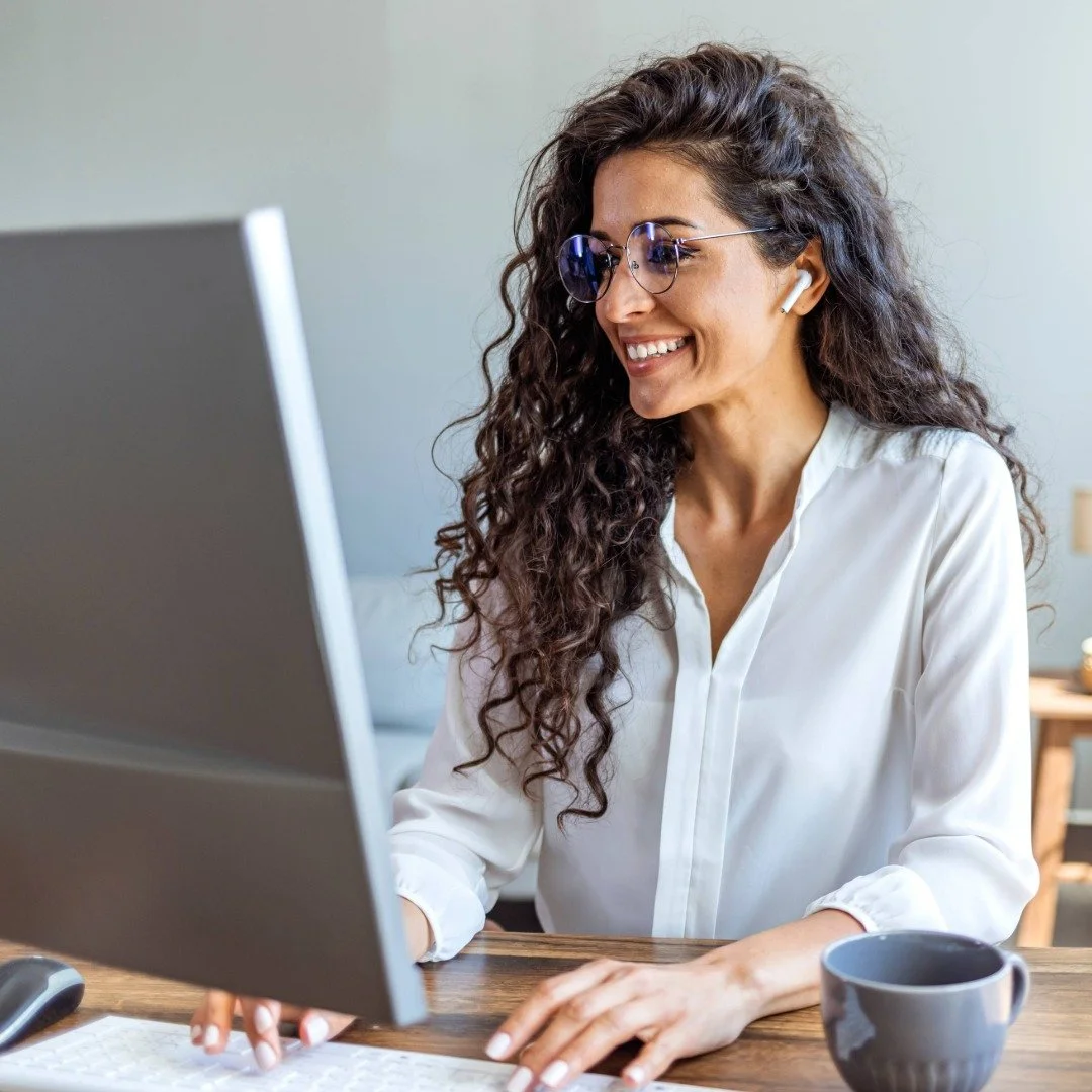 A person, smiling while working on a computer at a desk, talking with a therapist.