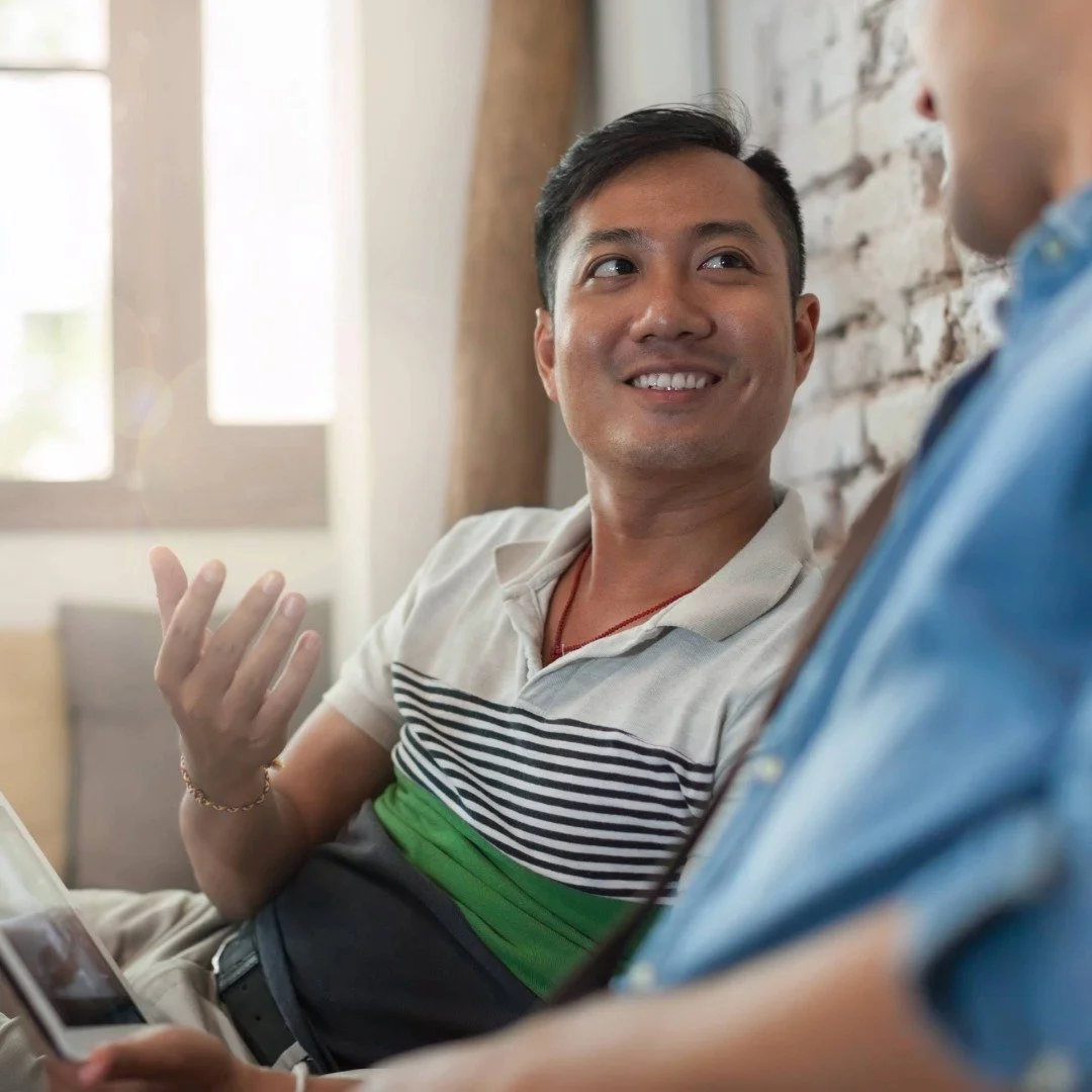 Two people having a conversation, one is smiling and gesturing with his hand, while the other is holding a phone.