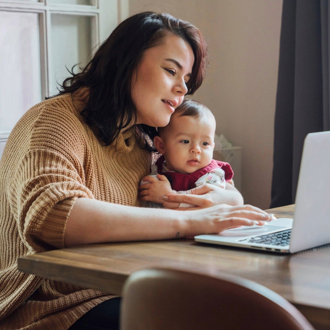 A mom and a baby sitting at a table looking at a laptop in a cozy home, while engaging in a therapy session.
