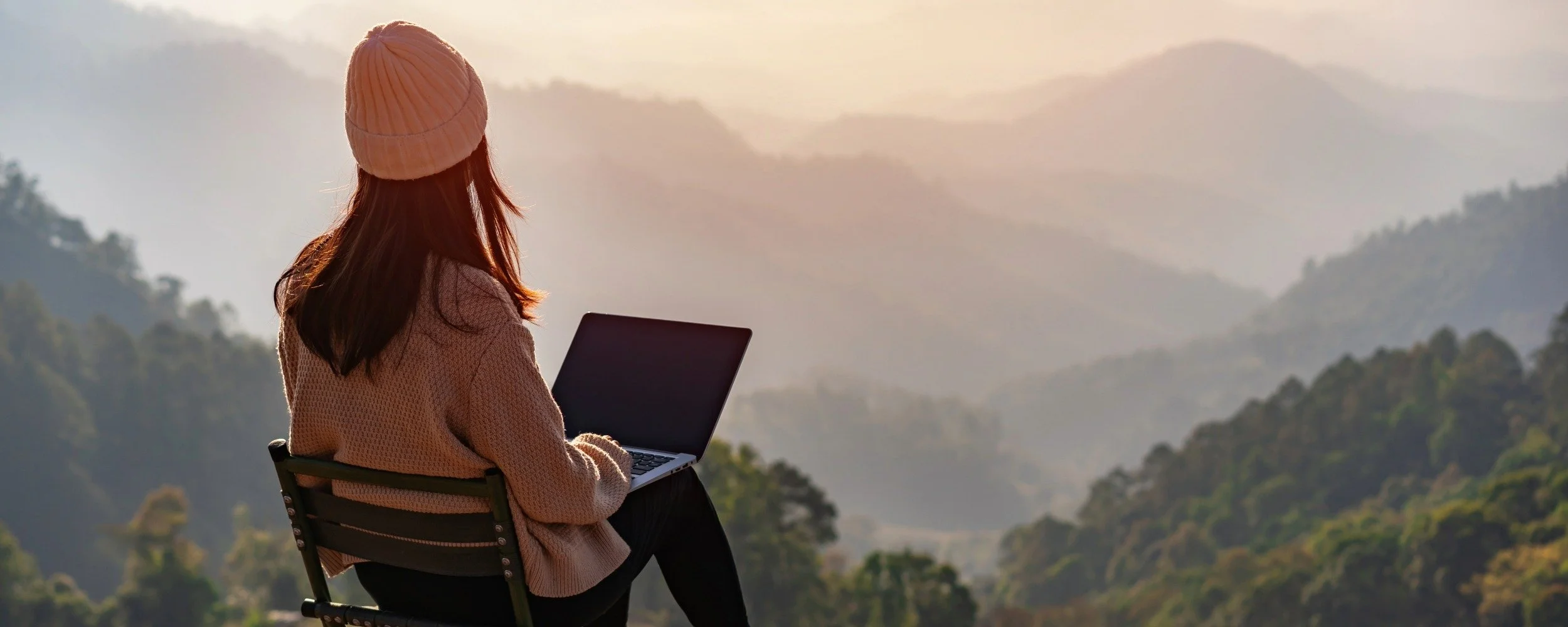 A person working on vacation on a laptop overlooking the mountains