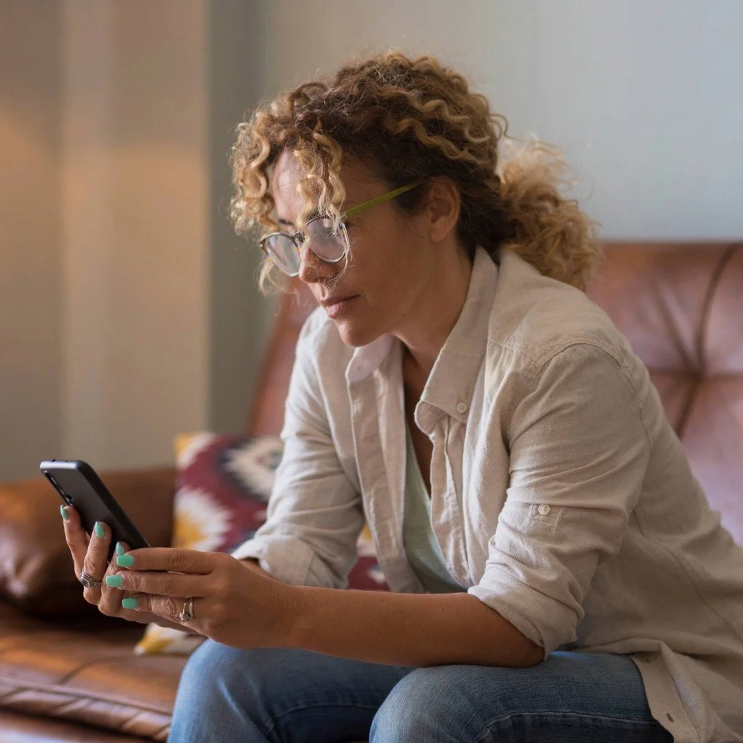 A person sitting on a couch, looking at their phone, engaged in a phone therapy session.