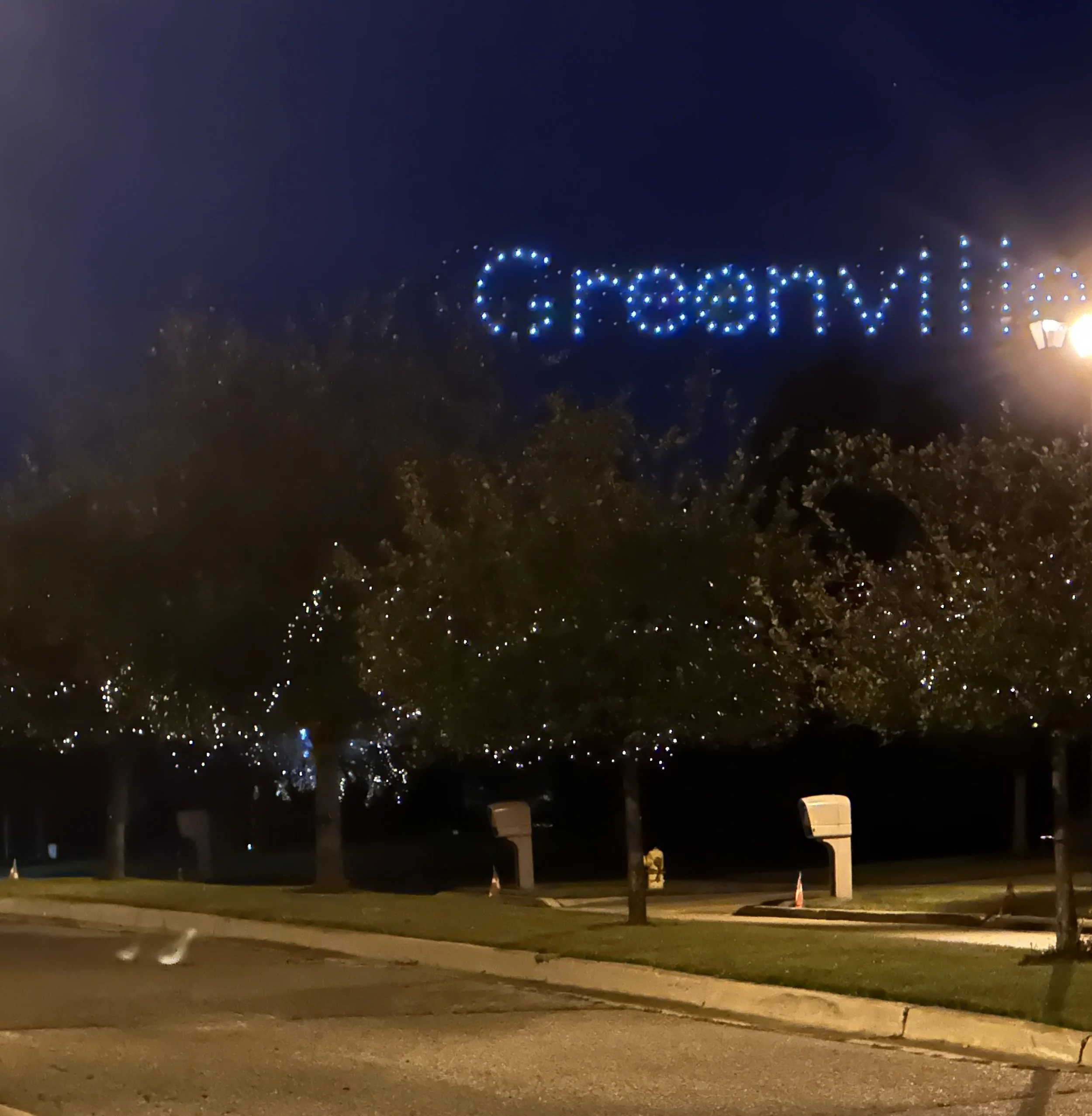 Tree decorated with Christmas lights, with a sign in the sky that reads 'Merry Christmas' in blue lights.