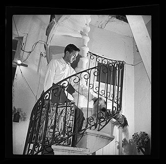 A man cleaning or tending to a potted plant on a decorative spiral staircase balcony in a building interior.