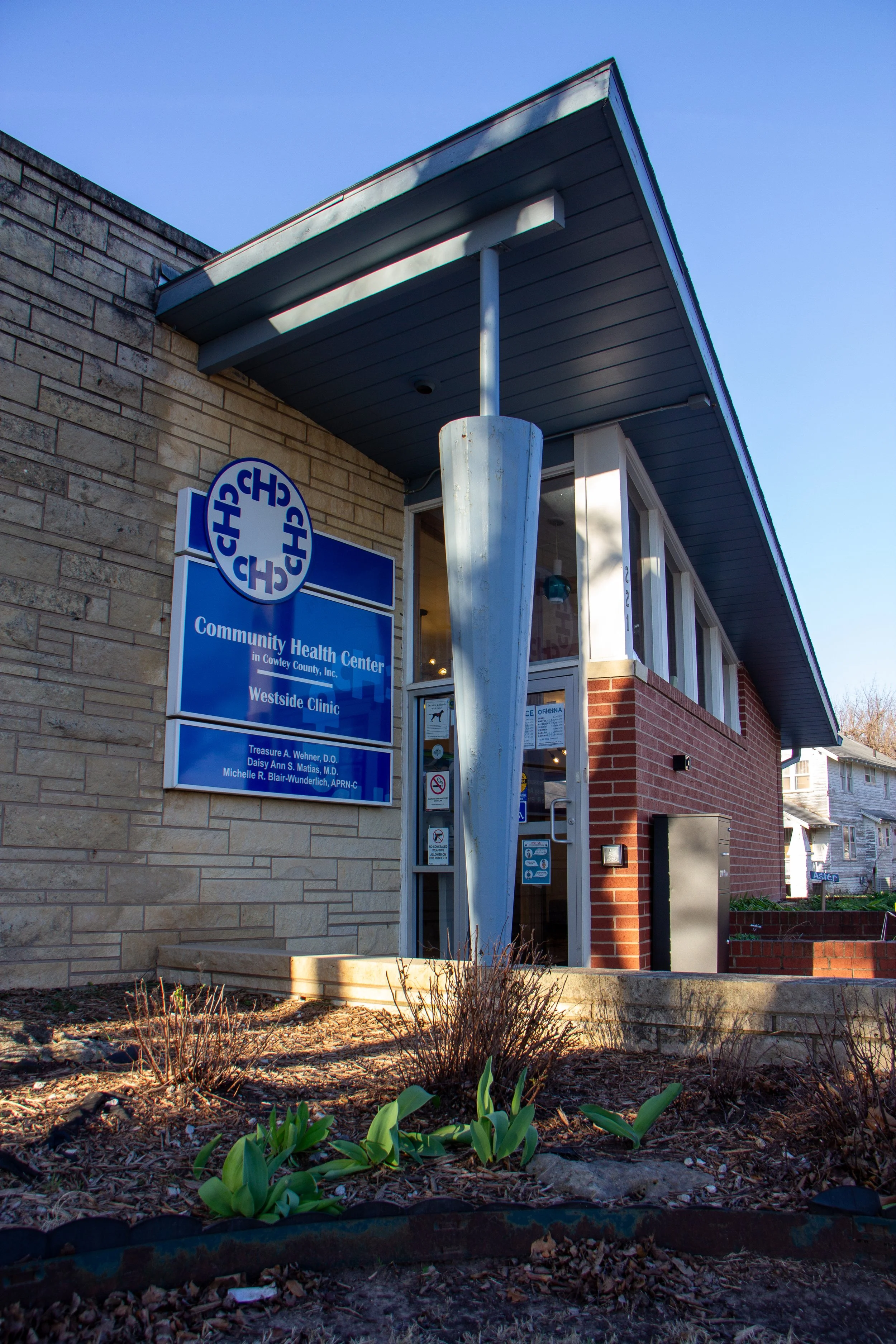 A building with a blue sign, brick and stone exterior, and a small garden in front.