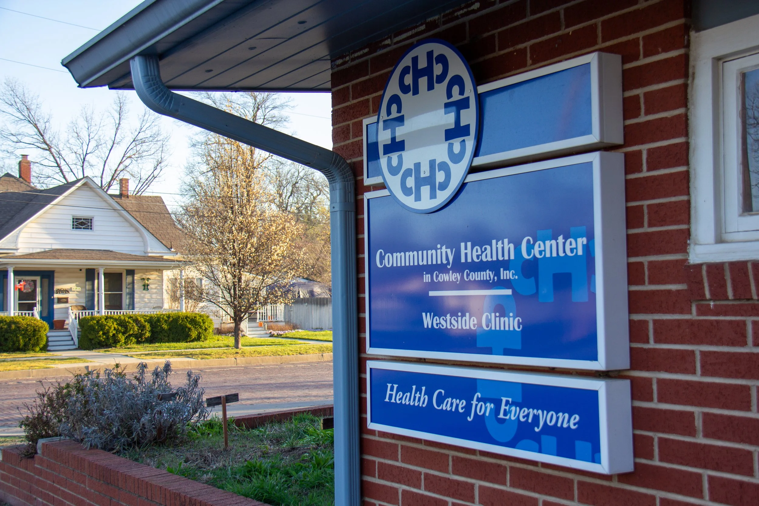 Sign for Community Health Center in Cowley County, Inc., Westside Clinic, with slogan 'Health Care for Everyone,' mounted on a brick wall outside a building