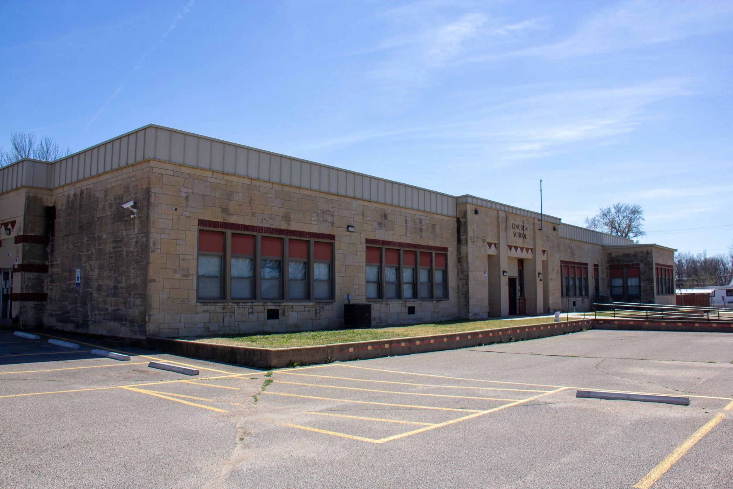 A single-story building with beige brick walls and large windows, labeled 'Lincoln School'.