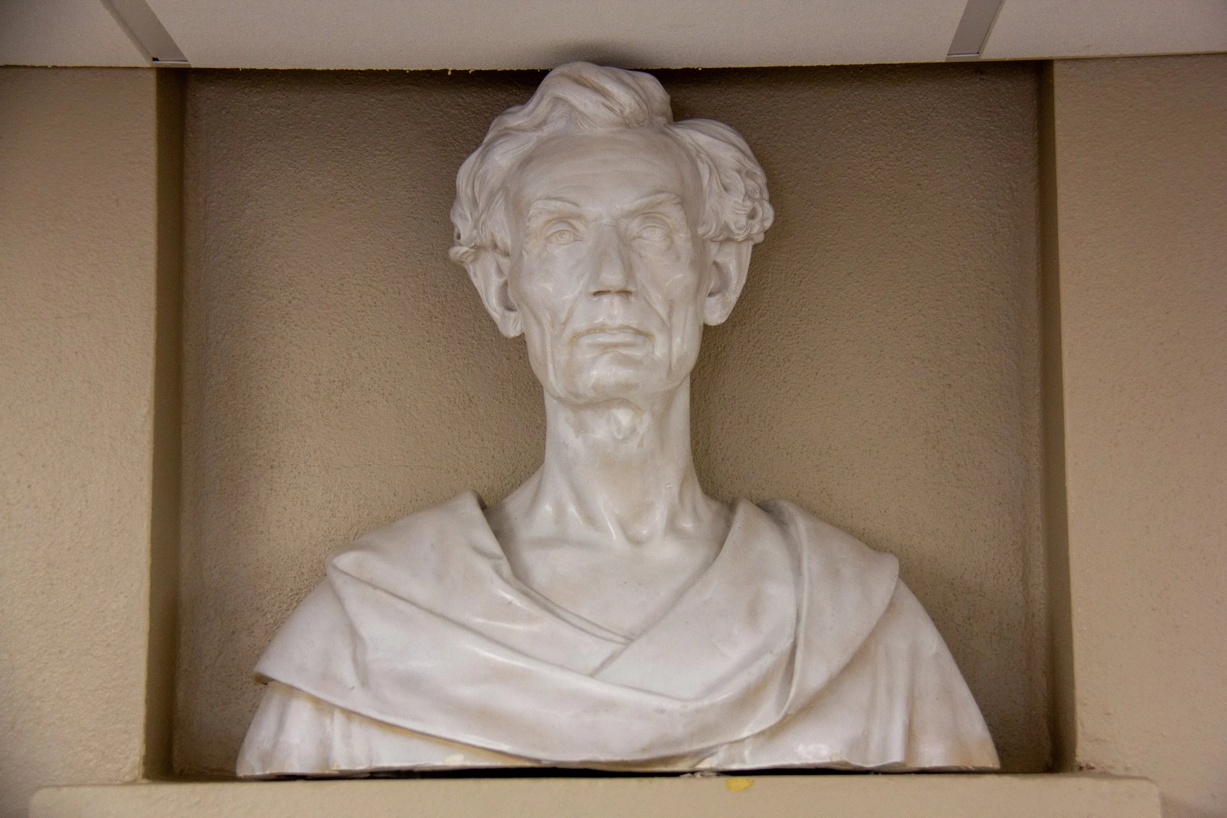 White bust of an elderly man with wavy hair, displayed in a recessed wall niche.