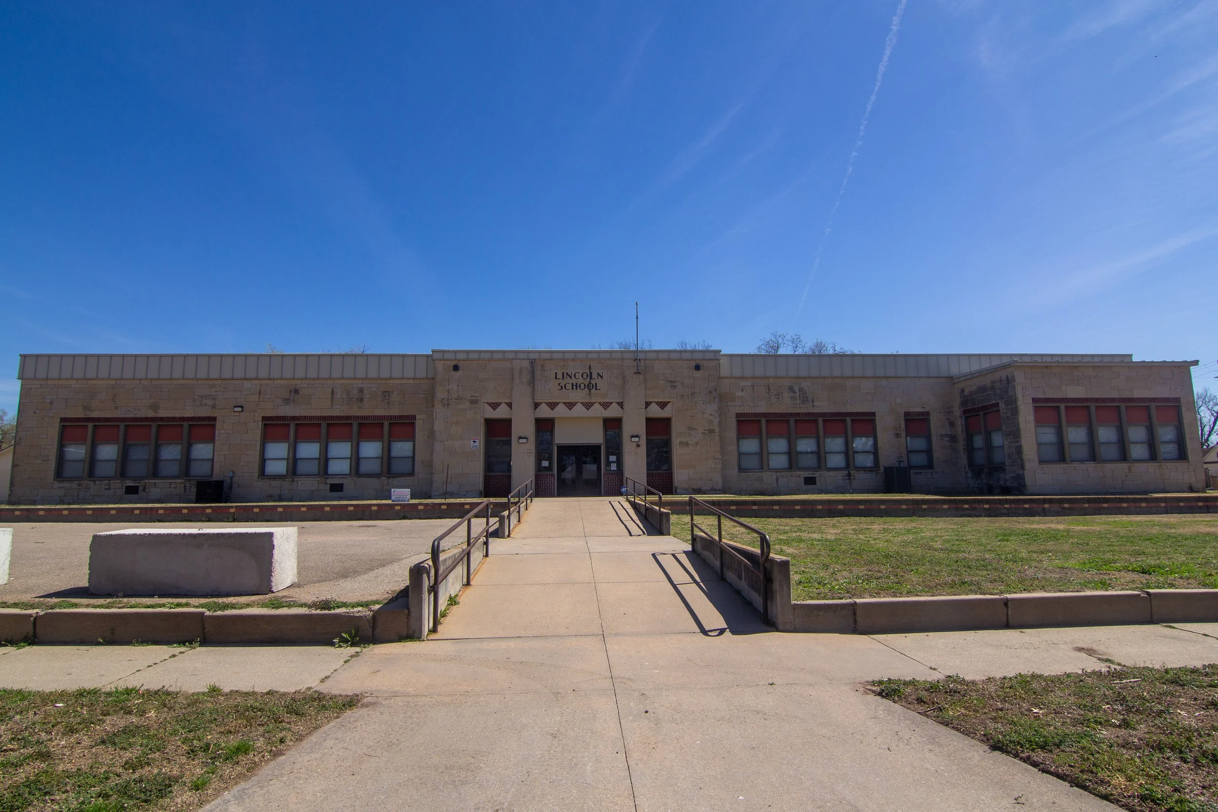 Front view of Lincoln Clinic with a central entrance, surrounded by grassy area, concrete walkways, and a bright blue sky.