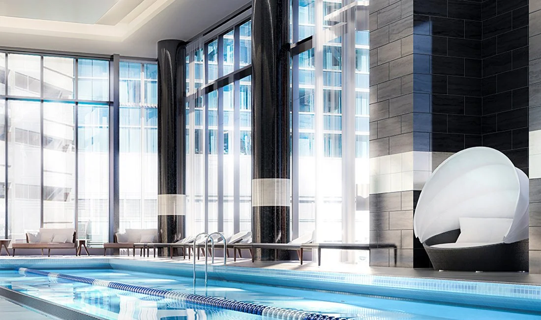 Indoor swimming pool area with large floor-to-ceiling windows, lounge chairs, and modern seating.