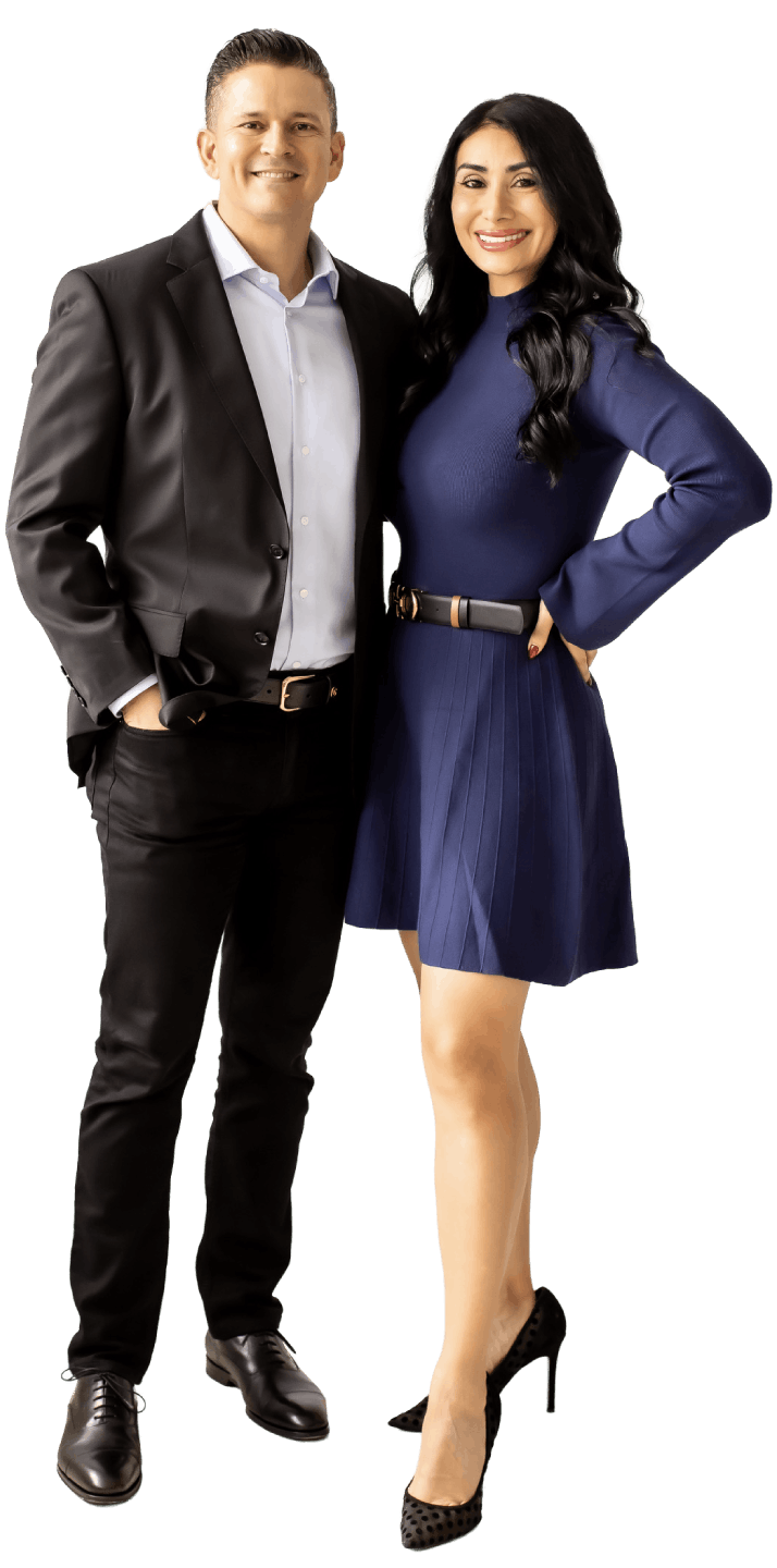 A man in a black suit and a woman in a blue dress standing together smiling, with her hand on her hip.