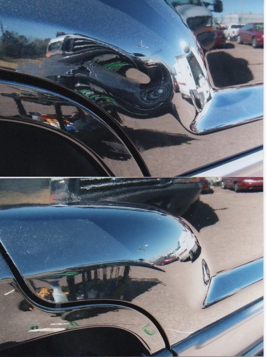 Close-up view of a black motorcycle or car with shiny reflective surface, showing reflections of the surrounding parking lot and vehicles.