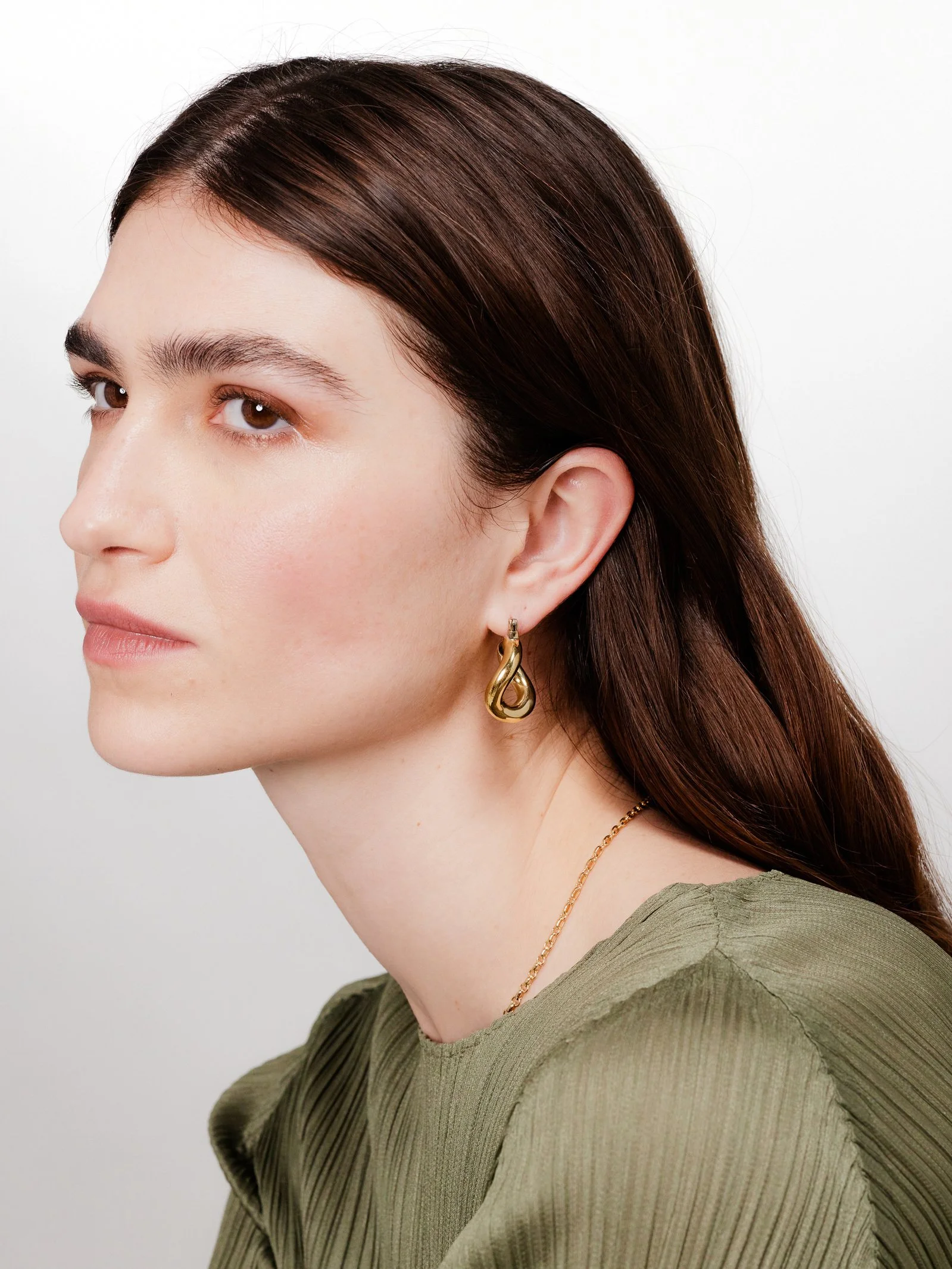 Close-up side profile of a woman with brown hair wearing gold earrings and a green top.