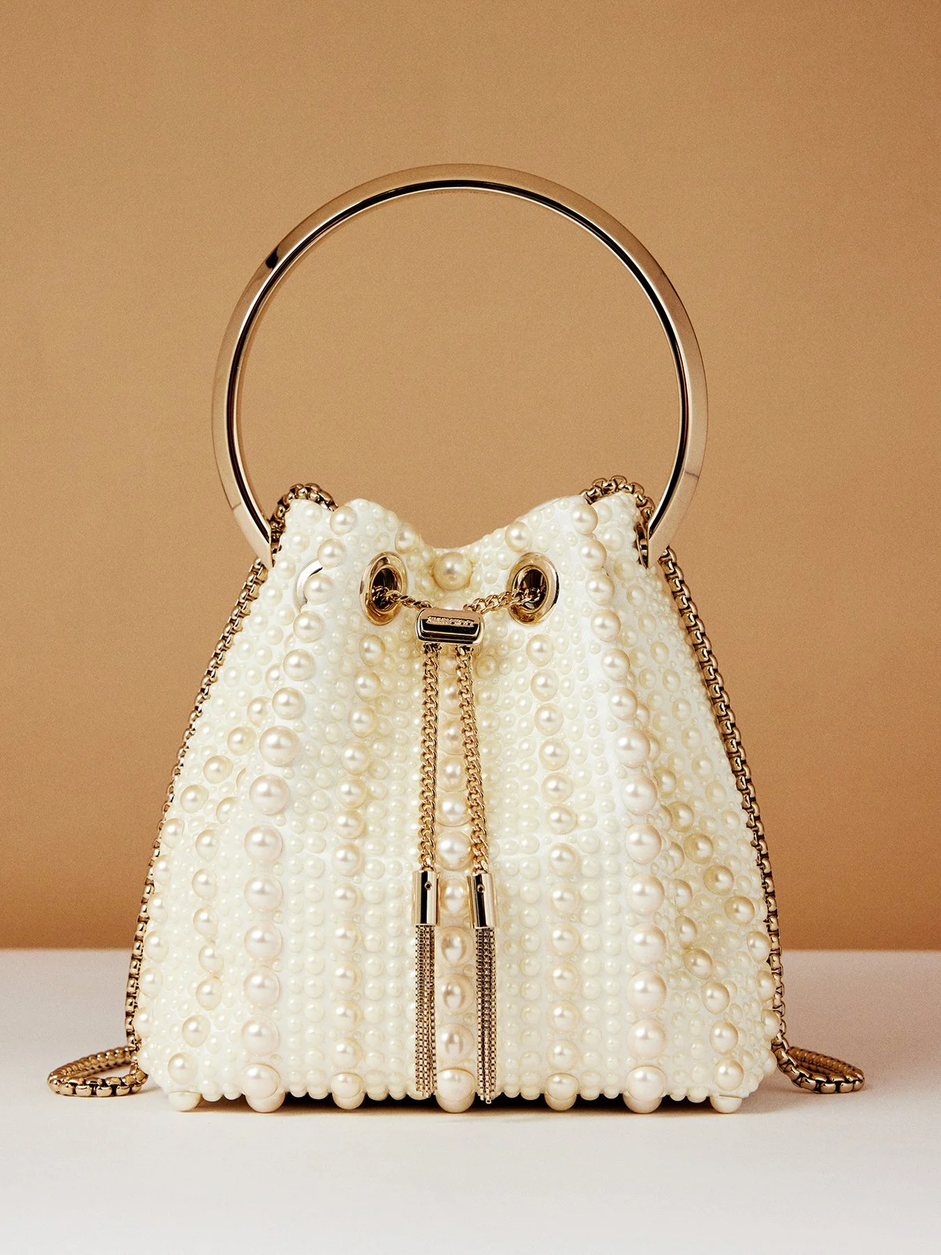 A white handbag decorated with pearls and gold accents, featuring a round gold handle and chain details.
