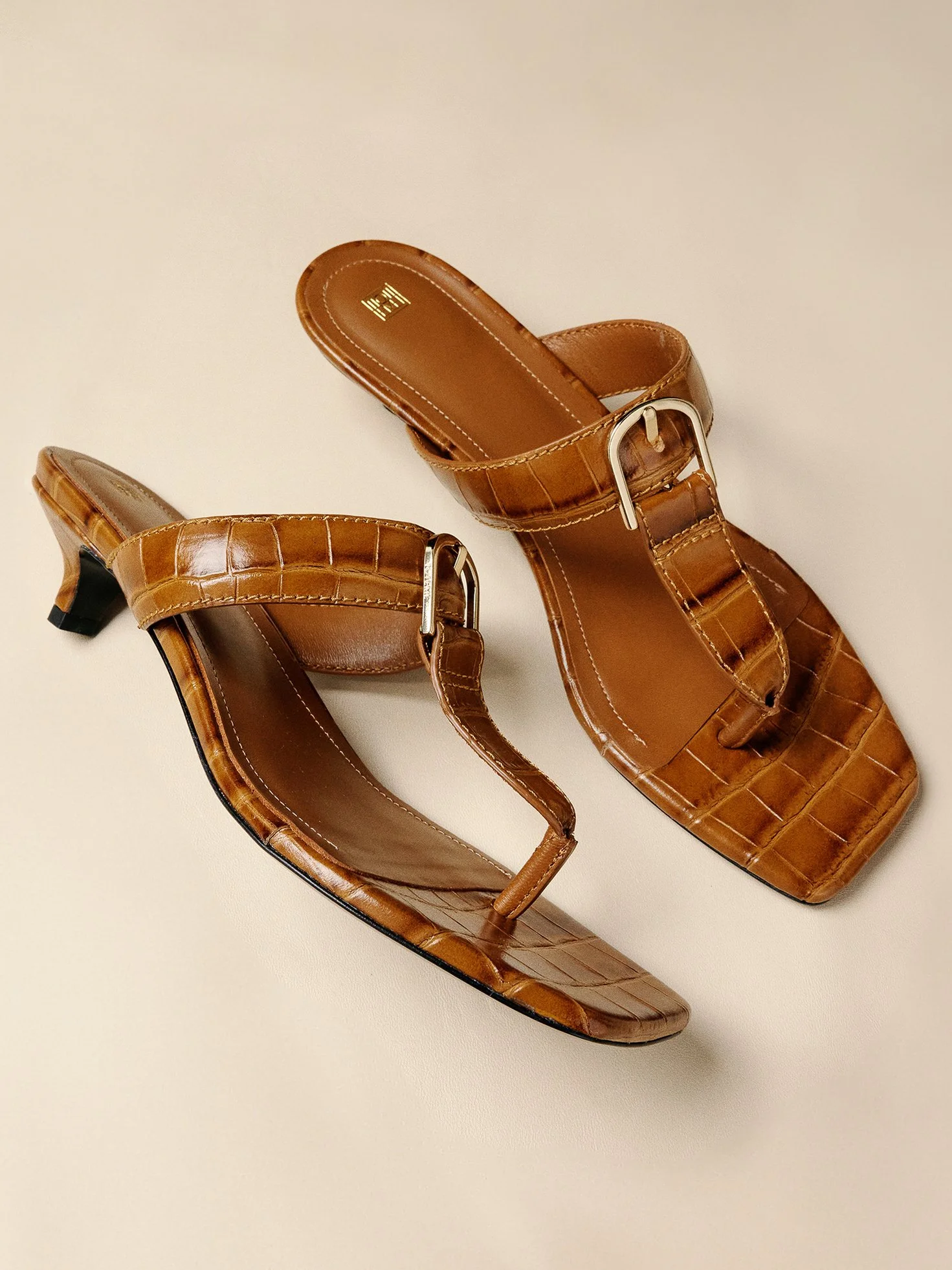 Brown heeled sandals with crocodile pattern and silver buckles on a white surface.