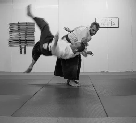 Two martial artists practicing Aikido in a dojo, with one performing a throw on the other.