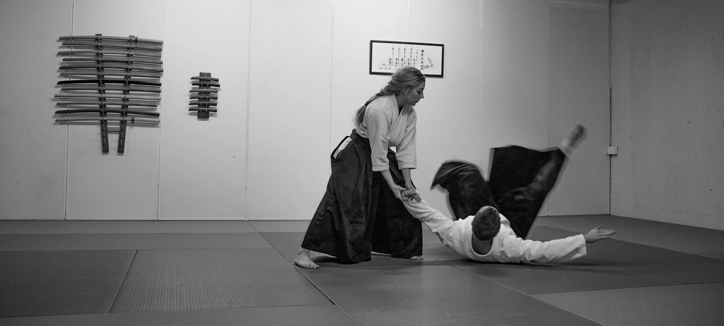 A women and a man  practicing martial arts in a dojo, one in the process of throwing the other on the mat.